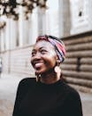 Smiling woman wearing vibrant headscarf and earrings, captured in an urban street setting.